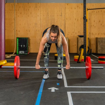Femme dans salle de sport avec barre disque musculation rouge
