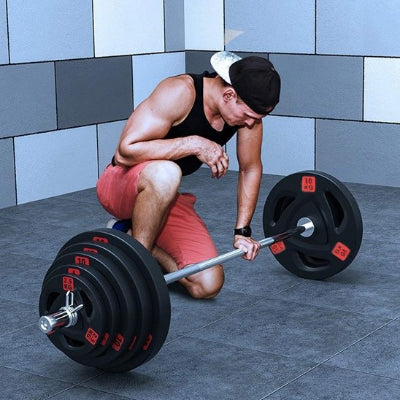 L'homme à genoux tient la barre avec disque musculation 
