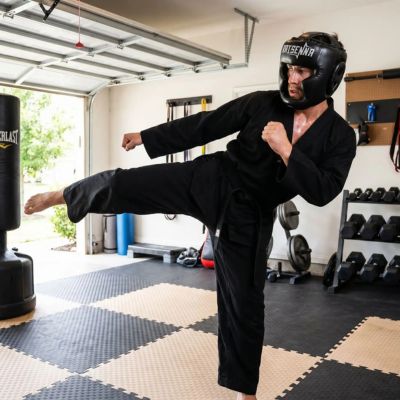 homme dans son garage pratique taekwondo avec casques de boxe