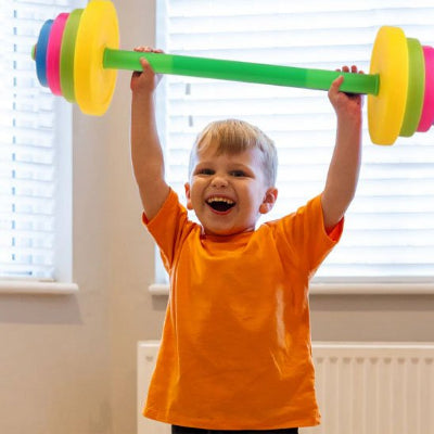 Petit garçon chandail orange soulève en souriant son haltère 